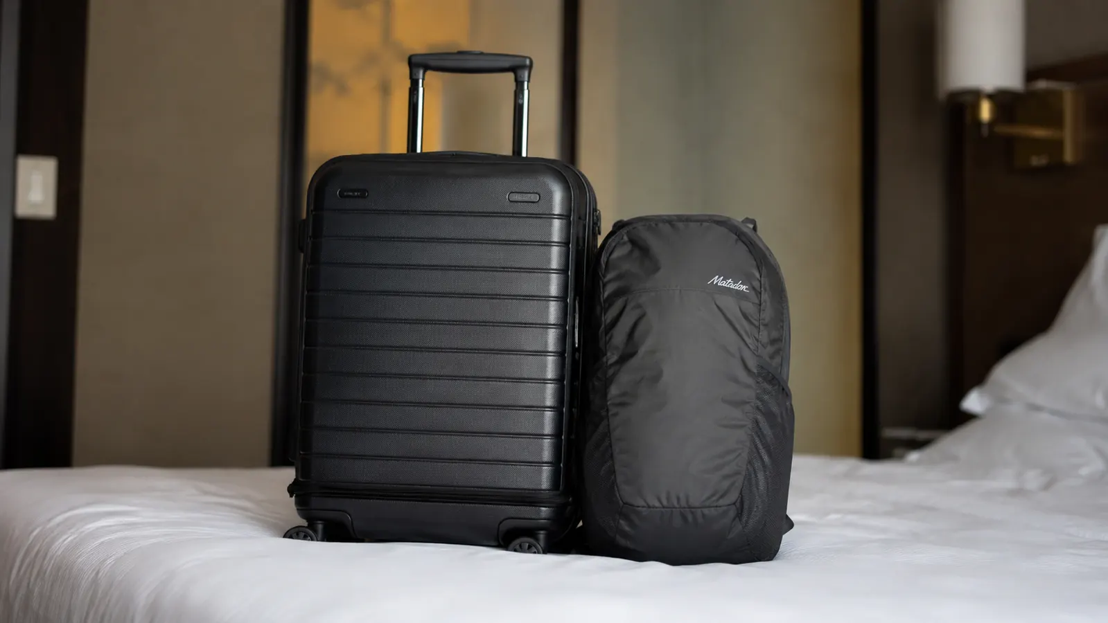 Packed daypack beside a roller carry-on suitcase showing size comparison
