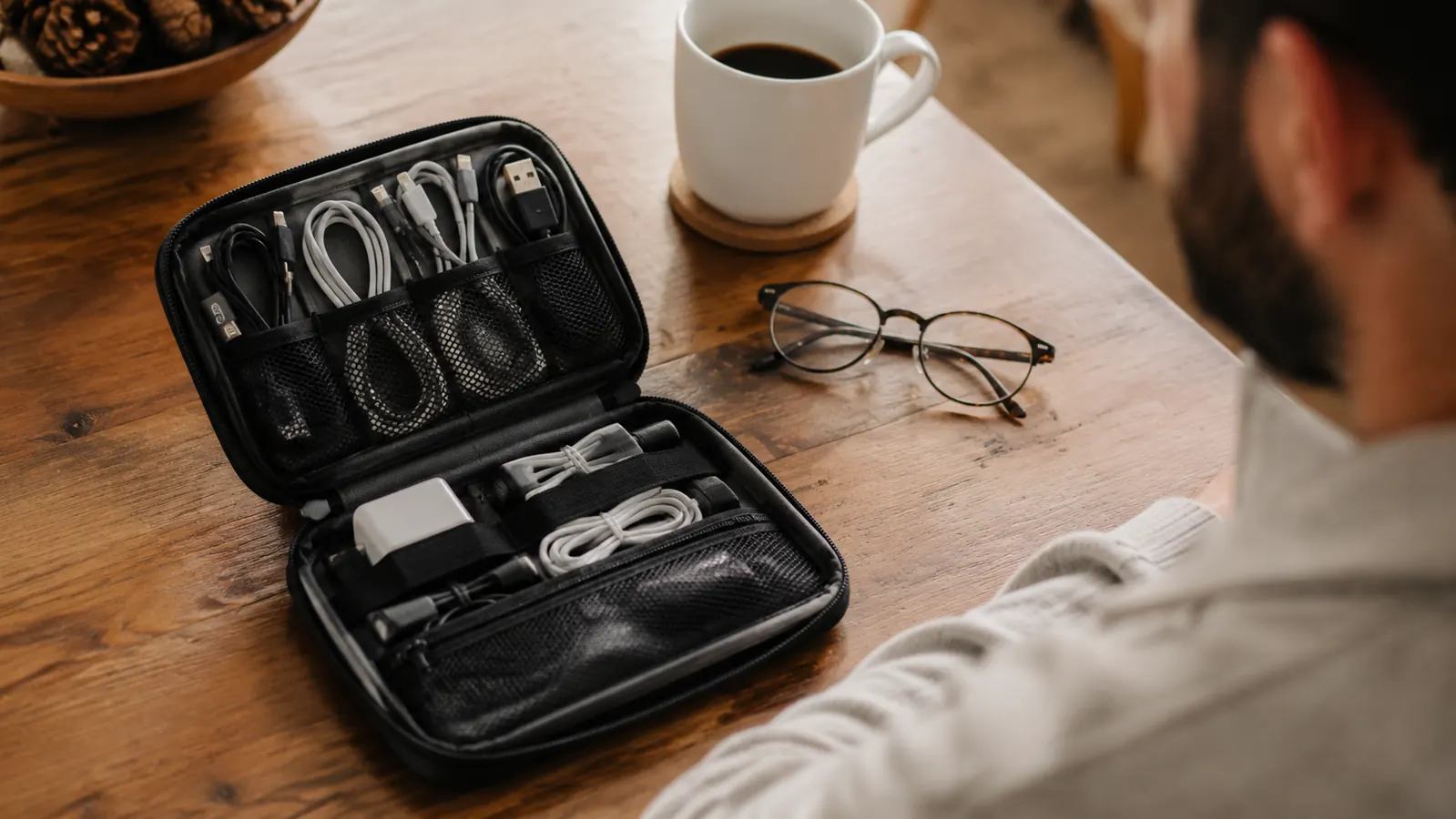 Cable organizer pouch laid flat on wooden kitchen table with coffee mug nearby, open to show contents organized inside