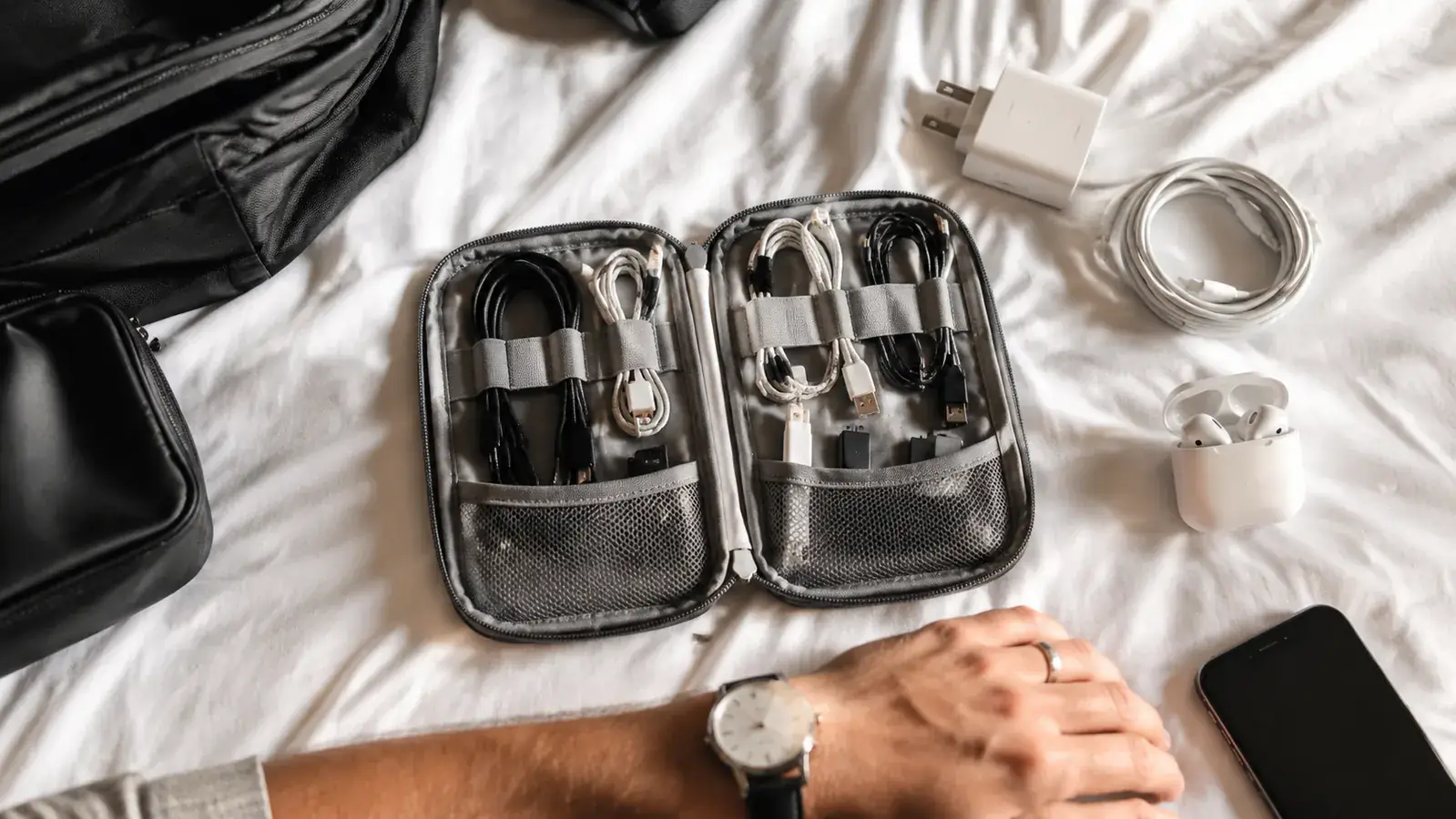 Open travel bag on a bed with cables, chargers, and adapters neatly laid out ready to pack