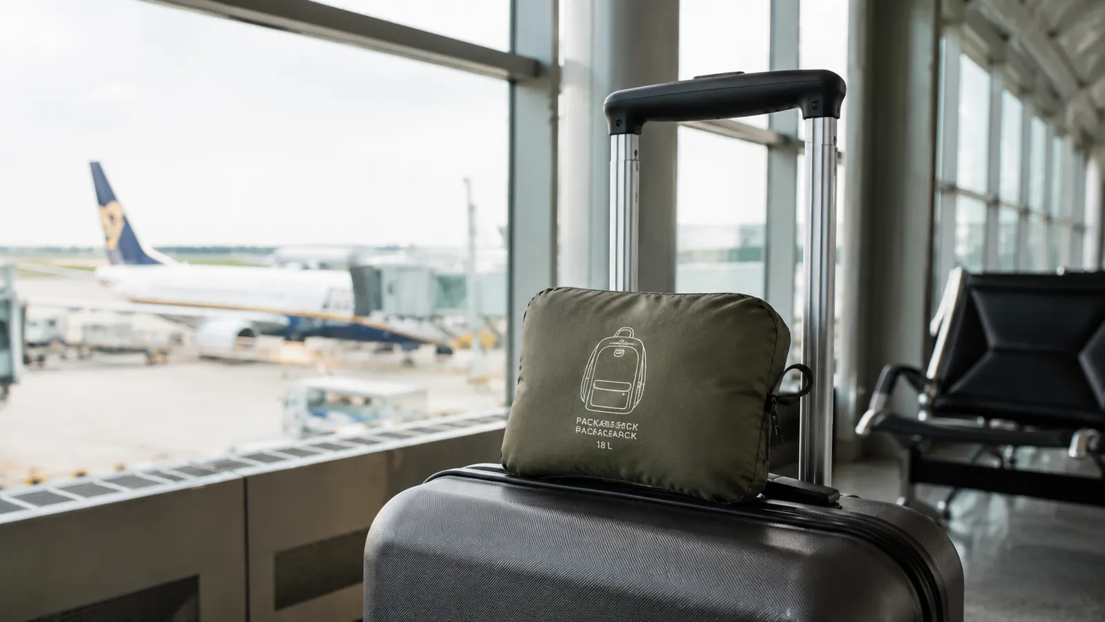 Packable backpack folded into its pouch resting next to a carry-on bag