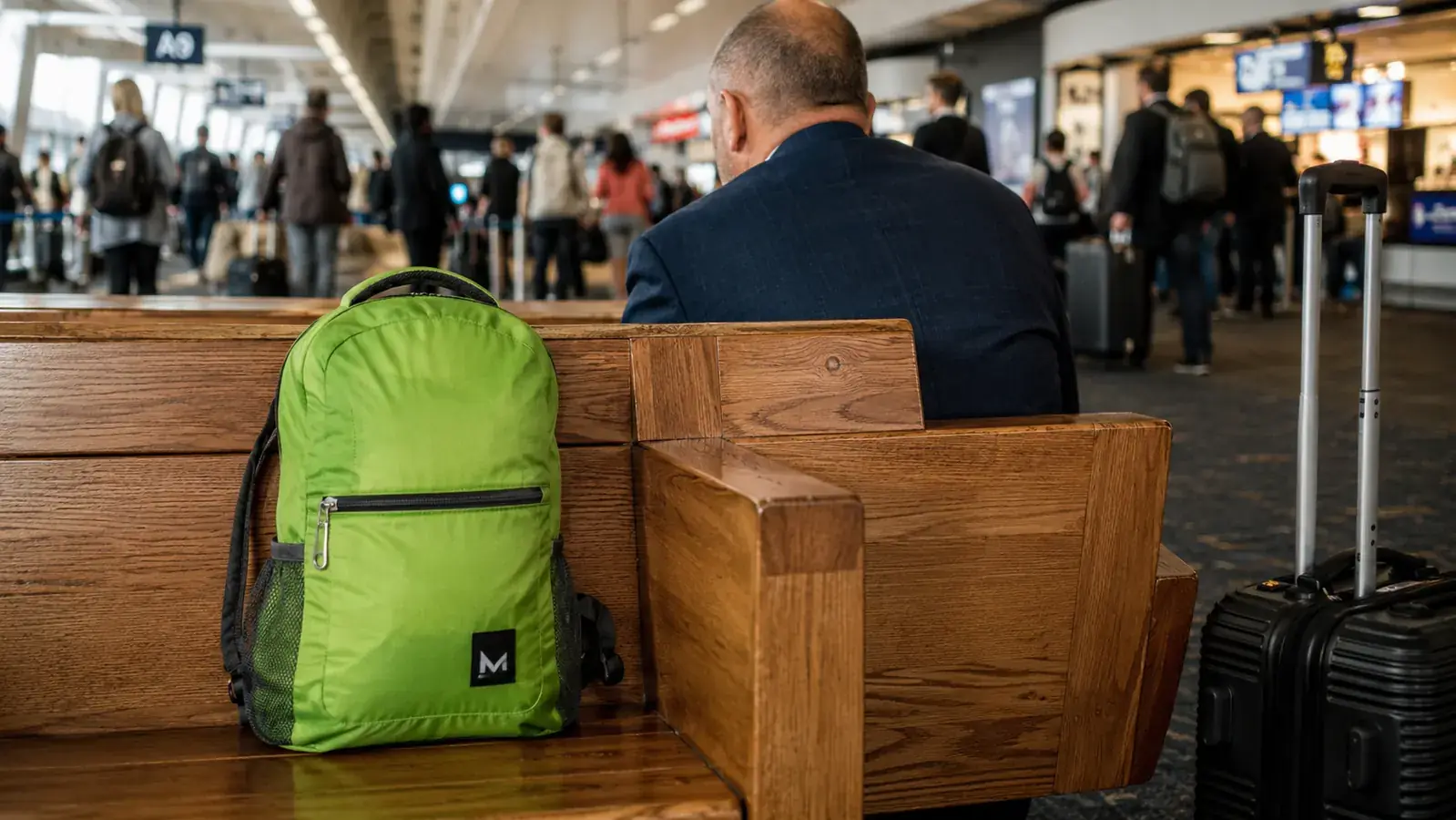ZOMAKE packable daypack on a wooden bench at an airport gate, overhead bin visible in background