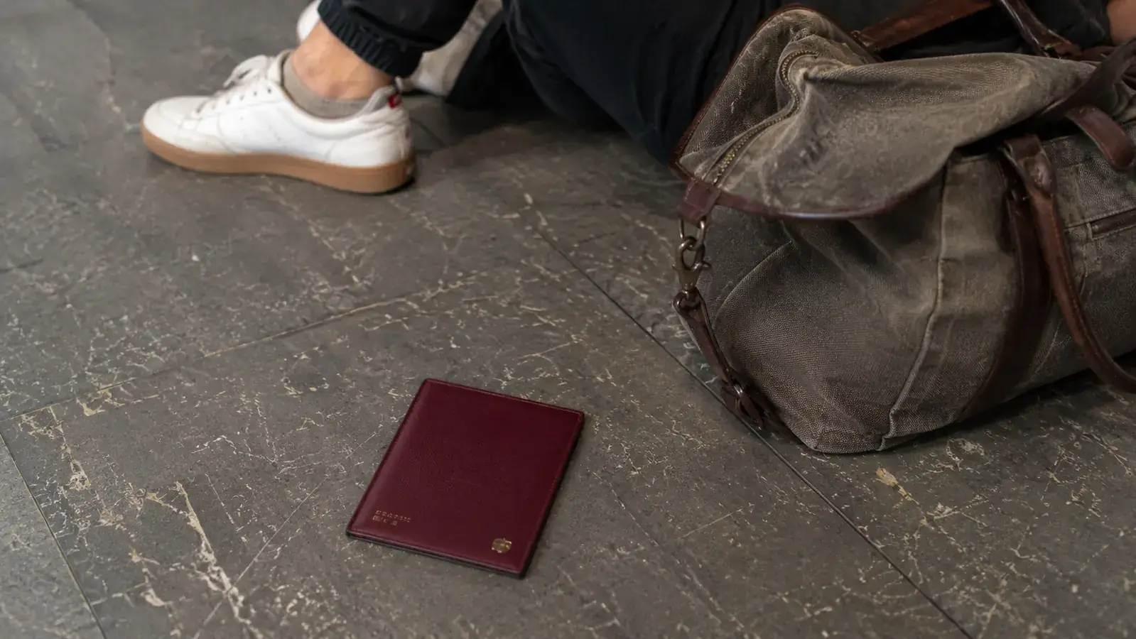 ZOPPEN RFID passport wallet lying on a crowded airport terminal floor next to a travel bag, honest and unglamorous real-world setting